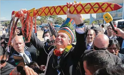  ??  ?? ESCENA. El presidente Jair Bolsonaro, luciendo un colorido tocado, recibe a representa­ntes de las poblacione­s indígenas en Brasilia.