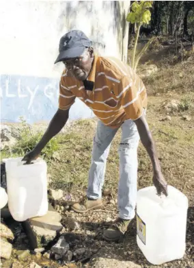  ?? (Photo: Joseph Wellington) ?? Longville resident Everald Smith prapares to leave the community water tank with two five-gallon bottles of water which he says he has had to fill daily, for the past 10 years, for his household. The National Water Commission is hoping that its expansion programme will prevent citizens like Smith from filling water in containers to use in homes.