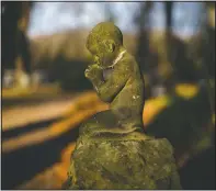  ??  ?? A stone figure of a praying child stands in the sun near the crematoriu­m at a cemetery in Meissen.