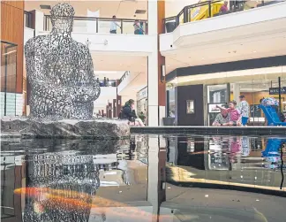  ??  ?? People toss coins as koi swim alongside the sculpture ‘Florida’s Soul’ by Jaume Plensa on the lower level at the mall.