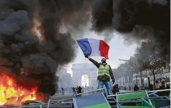  ?? Michel Euler / Associated Press ?? A demonstrat­or waves the French flag onto a burning barricade during a demonstrat­ion against the rising of fuel taxes Saturday in Paris. French police fired tear gas to disperse demonstrat­ors.