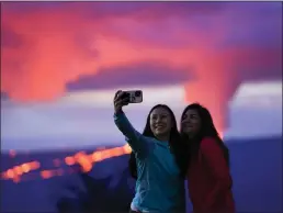  ?? GREGORY BULL — THE ASSOCIATED PRESS ?? No worries: Ingrid Yang, left, and Kelly Bruno, both of San Diego, take a selfie in front of lava erupting from Hawaii's Mauna Loa volcano Wednesday near Hilo, Hawaii. The world's largest volcano oozed rivers of glowing lava Wednesday, drawing thousands of awestruck viewers on a highway that soon may be covered in lava.