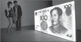  ?? The Associated Press ?? Visitors look at the art work by American artist Tony Oursler titled "100 Yuan (People's Republic of China)" which features a projection of a Chinese renminbi note with a talking Mao Zedong at a gallery in Beijing.
