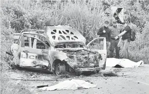  ?? — Gambar AFP ?? DISERANG GANAS: Ejen polis melihat trak peronda polis yang hangus dan dua mayat mangsa yang ditutup dengan kain putih sejurus serangan di Caldono, Cauca kelmarin.