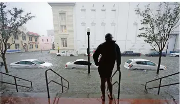  ?? FOTO: GERALD HERBERT/AP/DPA ?? Ein Mann steht auf den Stufen eines Gebäudes in Pensacola, Florida, und blickt auf eine überschwem­mte Straße. In vier Stunden fiel in der Stadt während des Sturms so viel Regen wie sonst in vier Monaten.