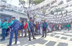  ?? — AFP photo ?? Voters wait in line outside a polling station while security police officials watch over them in Dhaka.