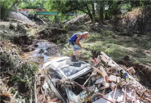  ?? GABRIELA CAMPOS/THE NEW MEXICAN ?? Billy Lacasella inspects a Honda lodged in an arroyo on his property in La Cienega that was carried down by floodwater from Monday night’s storm. First responders carried out several rescues Monday night.