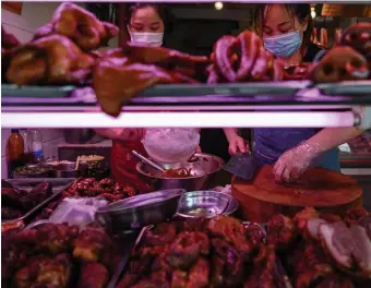  ?? GETTY IMAGES ?? TRIMMING THE FAT: Vendors wearing face masks prepare meat in a market in Wuhan on Monday. The City of Wuhan has banned eating wild animals and Chinese farmers are being offered cash to quit breeding exotic animals.