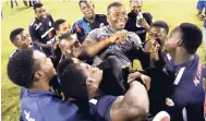  ??  ?? Jamaica College’s coach Miguel Coley is hoisted by his players after the Old Hope Road-based school won the ISSA/FLOW Walker Cup at the National Stadium yesterday.