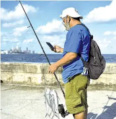  ??  ?? A Cuban fisherman uses his cell phone to connect to the internet at the Malecon in Havana.