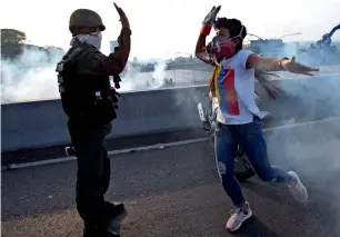  ?? AP ?? An opponent to Maduro high fives a rebel soldier on a highway overpass outside La Carlota air base amid tear gas fired by loyalist soldiers inside the base in Caracas, Venezuela, on Tuesday. —