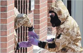  ?? MATT DUNHAM THE ASSOCIATED PRESS ?? Specialist team members in military protective suits use a jar in the front doorway as they search the fenced off John Baker House for homeless people in Salisbury, England, Friday.