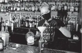  ?? [CARLOS OSORIO/ASSOCIATED PRESS] ?? Sugar House bartender Shelby Minnix creates a Lavender Lemonade cocktail in a to-go bottle in Detroit. Dave Kwiatkowsk­i, who owns the Sugar House, normally employs a staff of 16, but for now, it’s just him at the door and a bartender making drinks.