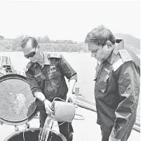  ?? — Gambar Bernama ?? PERIKSA: Xavier (kanan) melihat minyak diesel yang dibawa oleh sebuah kapal kargo yang berjaya ditahan di Pulau Redang di Setiu, semalam.