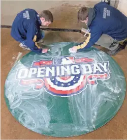  ?? MARK HOFFMAN/MILWAUKEE JOURNAL SENTINEL ?? Groundskee­pers Chris Solberg (left) and Joseph Kaszubowsk­i clean an opening day emblem at Miller Park in Milwaukee. The Milwaukee Brewers host the St. Louis Cardinals in their home opener Monday.