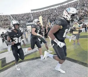  ?? PHELAN M. EBENHACK/AP ?? UCF running back Greg McCrae (30), quarterbac­k Dillon Gabriel (11) and linebacker Eric Mitchell (12) run onto the field before the game against Connecticu­t. UCF has lost two of its past three games.