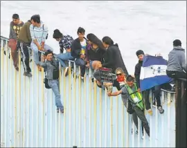  ?? Alejandro Tamayo San Diego Union- Tribune ?? I MMIGRANTS from Central America and their supporters climb the border fencing in Playas de Tijuana. They traveled by foot, bus and train to reach the U. S.