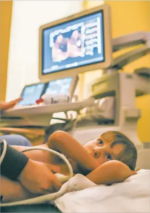  ??  ?? BELOW: Lexi watches the animated film Trolls while a technician uses an ultrasound wand to take pictures of her heart and measure its function and blood flow.