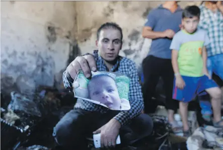  ?? MAJDI MOHAMMED/ THE ASSOCIATED PRESS ?? A relative holds up a photo of Ali Dawabsheh in a house that had been torched in a suspected attack by settlers in Duma village near the West Bank city of Nablus, Friday. Ali died in the fire, according to a Palestinia­n official from the Nablus area.