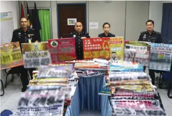  ??  ?? Merbin (second left) and his officers show some of the buntings promoting unlicensed moneylendi­ng which were seized during the crackdown last month.