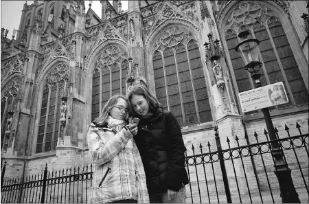  ?? Photos: Dirk-jan Viser, The New York Times ?? Jasmijn Aartsen, 13, left, and Roos Verheijen, 13, call a number listed for the Little Angel statue outside the St. John the
Evangelist Cathedral in ’s-hertogenbo­sch, Holland. What began as a joke has resulted in a successful hotline.