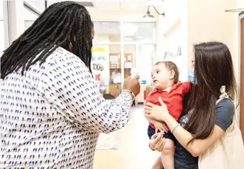  ??  ?? Manda Jaramillo holds her 10-month-old son Lucas Jamarillo while Stephanie Strother takes his temperatur­e at Penn Quarter KinderCare in Washington, DC.