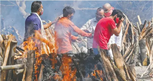  ?? PRAKASH SINGH / AFP VIA GETTY IMAGES ?? A man performs last rites Tuesday for a relative amid the funeral pyres of people who died from COVID-19 during mass cremation in New Delhi. The raging pandemic in India has helped push global infection rates to record levels.