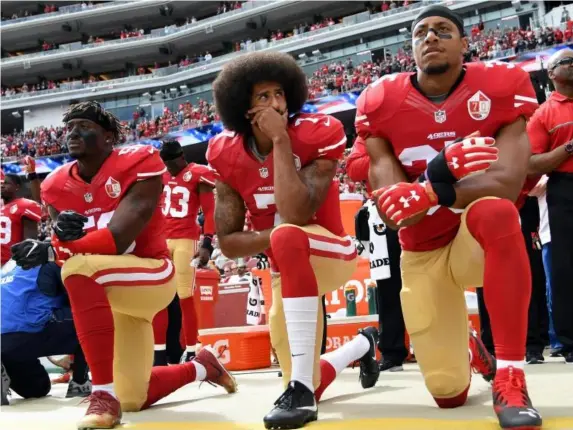  ?? (Getty) ?? Eli Harold, Colin Kaepernick and Eric Reid of the San Francisco 49ers kneel on the sideline during the anthem