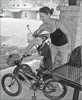  ?? [BARBARA J. PERENIC/DISPATCH PHOTOS] ?? Brenda Young helps her son Zachary, 5, get ready to ride his bike at Pierce Field in Grandview Heights. The family supports a law being considered in Grandview that would require bicyclists younger than 18 to wear a helmet.