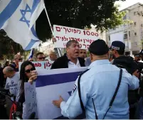  ?? (Baz Ratner/Reuters) ?? POLICEMEN FACE employees of Israel Broadcasti­ng Authority as they hold Israeli flags and protest against the Histadrut labor federation outside their headquarte­rs in Tel Aviv on March 19.