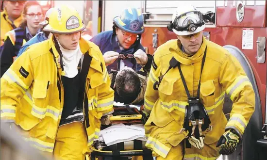  ?? Haley Nelson/Post-Gazette photos ?? A firefighte­r is taken to an ambulance after battling a blaze at a three-story house in the 3900 block of Vinceton Street in Perry North on Friday evening.