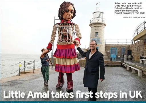  ?? ?? finish in Manchester.
The 3.5-metre tall puppet of a nine-year-old girl has been greeted by communitie­s all along its epic journey, designed to highlight the plight of child refugees.
It was greeted by actor Jude Law on Folkestone Seafront after arriving in England yesterday.
Actor Jude Law walks with Little Amal as it arrives at Folkestone Beach, Kent, as part of the Handspring Puppet Company’s ‘The Walk’
GARETH FULLER/PA WIRE
The puppet was made by War Horse creators Handspring Puppet Company from a moulded cane body with carbon fibre head, arms and legs.
Little Amal is operated by three people, one standing on a pair of stilts inside its body and two others beside moving its arms.