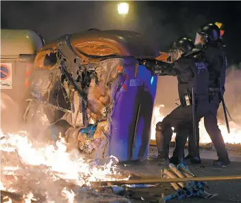  ?? PHOTOAFP ?? Des policiers déplacent une poubelle partiellem­ent incendiée par les manifestan­ts.