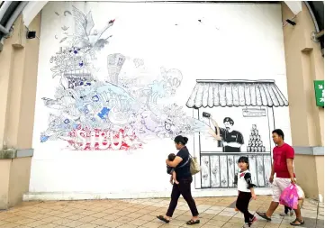  ??  ?? A woman and her family walk past the ‘Teh Tarik Doodle’ painting.