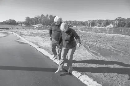  ?? ?? In their Willow Point neighborho­od, residents Scott and Susan Esslinger step over ever-present runoff from tides, rain and basements being pumped.“The water now comes up to the sea wall regularly,” Susan Esslinger said.