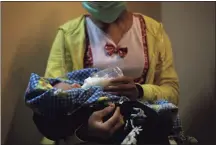  ?? Associated Press ?? A 17-year-old mother gives a bottle to her 2-week-old baby, whom she says was born as a result of a rape in Sumatra, Indonesia. She started working on a palm oil plantation as a young child to help her family survive.