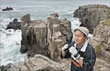  ?? JONATHAN KAIMAN/LOS ANGELES TIMES ?? Retired policeman Yukio Shige uses binoculars to find people preparing to commit suicide on Japan’s Tojinbo cliffs. Shige’s nonprofit has about 20 volunteers who keep a near constant watch out for people during daylight hours.