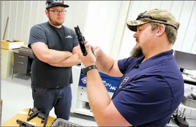  ?? NWA Democrat-Gazette/DAVID GOTTSCHALK ?? Guy Joubert (right) and Neal Trout inspect a Glock handgun’s polymer frame at Wilson Combat in Berryville. The company now offers custom gunsmith work on Glocks.