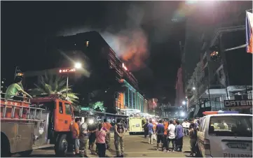  ??  ?? Evacuated employees and guests of hotels stand along a road and watch as smoke billows from a Resorts World building in Pasay City, Metro Manila.