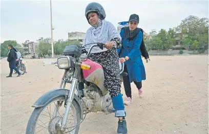  ?? Picture: AFP ?? IN THE SADDLE. Zainab Safdar, an instructor with the women-only Pakistani group ‘Rowdy Riders’, assists a student during a riding lesson in Karachi this week. Revving round a dusty oval in the heart of Pakistan’s largest city, women on motorbikes practise looping a row of safety cones.