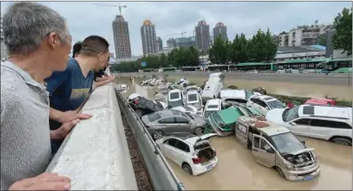  ?? (AFP) ?? People look out at cars sitting in floodwater­s after heavy rains hit the city of Zhengzhou in China’s central Henan province on Wednesday.