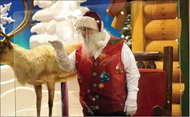  ?? (AP PHOTO/LYNNE SLADKY) ?? Santa Claus waves at children and their families from behind a transparen­t barrier at Bass Pro Shops last week in Miami. This is Santa Claus in the Coronaviru­s Age, where visits are done with layers of protection or moved online. Putting hundreds of kids a day onto your lap to talk directly into your face — that’s not happening.