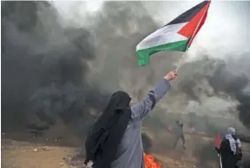  ?? THE ASSOCIATED PRESS PHOTOS ?? A woman waves a Palestinia­n flag in front of black smoke from burning tires during Friday’s protest at the Gaza Strip’s border with Israel.