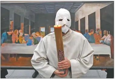  ?? (AP/Petr David Josek) ?? A participan­t wearing a mask holds a candle as he stands in front of a depiction of the painting the Last Supper.