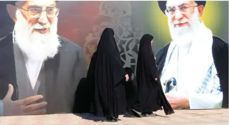  ?? (Ahmed Saad/Reuters) ?? WOMEN WALK past a poster depicting images of Shi’ite Iran’s Supreme Leader Ayatollah Ali Khamenei in Baghdad. Iran’s strategic expansion is on a scale no Persian regime has achieved since the Sassanid Empire.