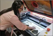  ?? LAUREN HALLIGAN - MEDIANEWS GROUP ?? Saratoga Custom Engraving owner Amanda VanPelt takes a freshly engraved piece of wood out of the shop’s laser engraving machine.