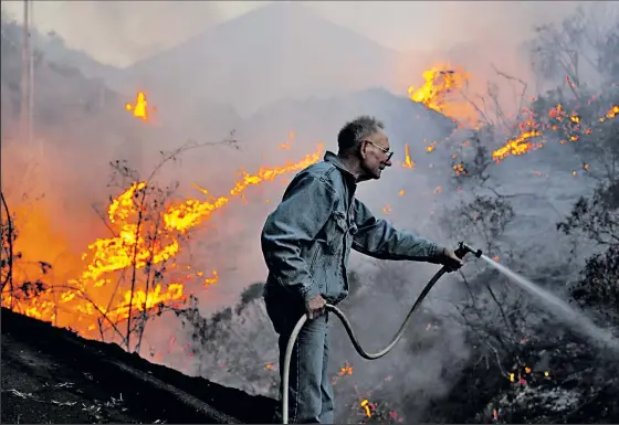  ?? LOS ANGELES TIMES ?? RICK LOOMIS James Harkins, 72, uses a garden hose to battle flames racing up a hillside toward his home in San Marcos, Calif. “What about my things, my memories, my things to pass on,” he said yesterday. “It’s mine. If it burns down, I don’t have a lot...