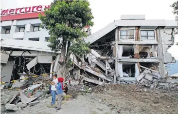  ?? [AP PHOTO] ?? Filipinos stand beside the heavily damaged Mercure hotel Thursday after a massive earthquake and tsunami hit Palu, Central Sulawesi, Indonesia.