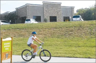  ?? (Special to NWA Democrat-Gazette/Xyta Lucas) ?? A bicyclist rides along the Wishing Springs trail below the buildings built on the landfill between the south end of Lake Bella Vista and Benton County 40.