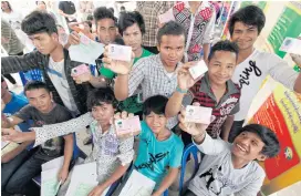  ??  ?? Migrant workers in the seafood-processing hub of Samut Sakhon show off identifica­tion cards issued under a 2014 programme to legalise foreign labourers.